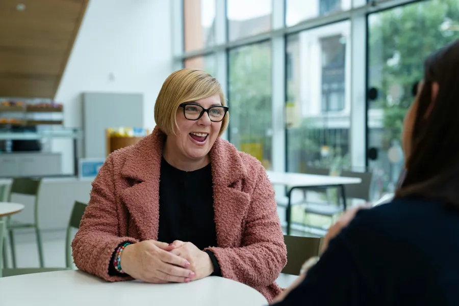 A support worker smiling and talking with someone across a table